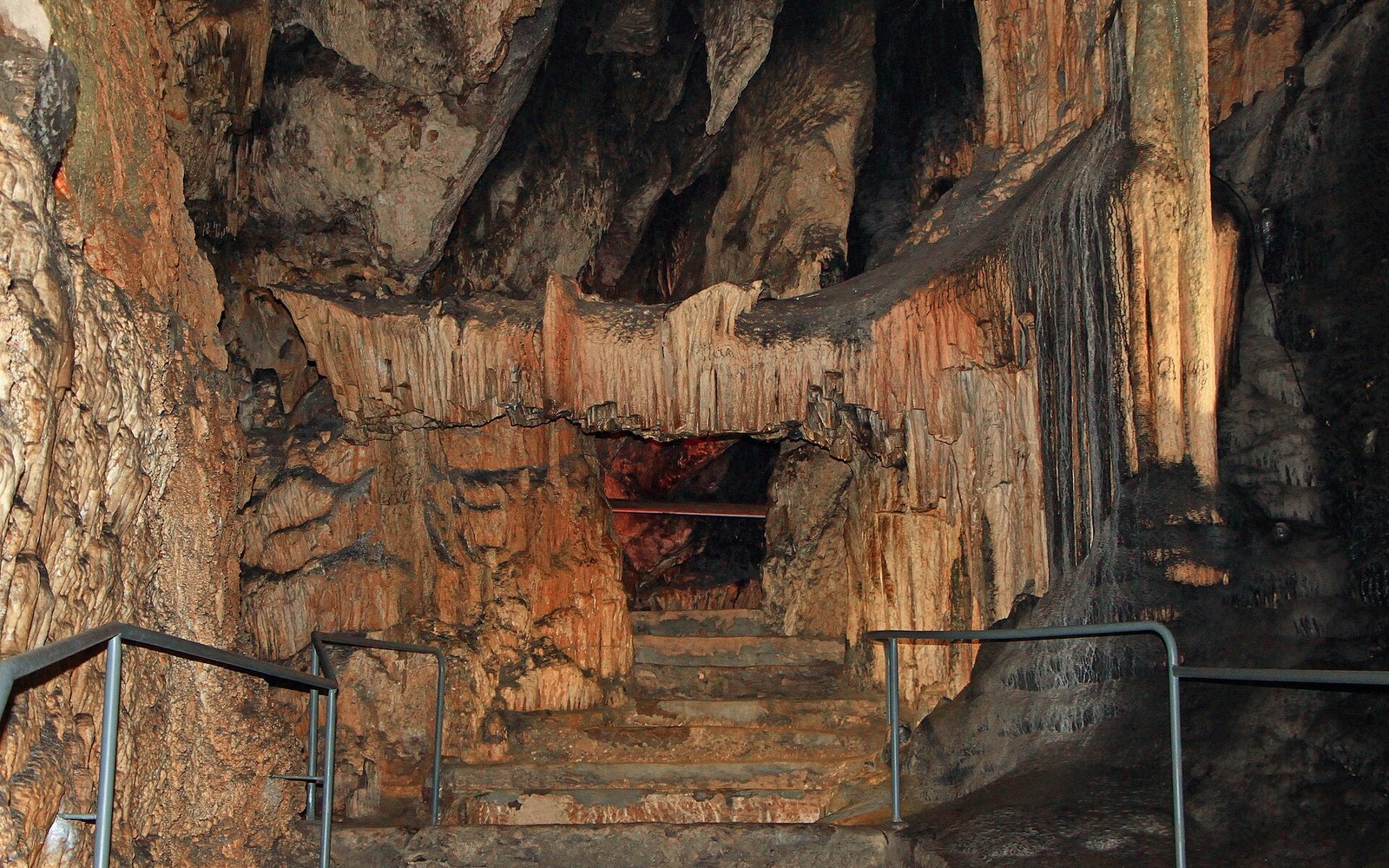 Stone staircase leads through a cave chamber lined with stalactite formations