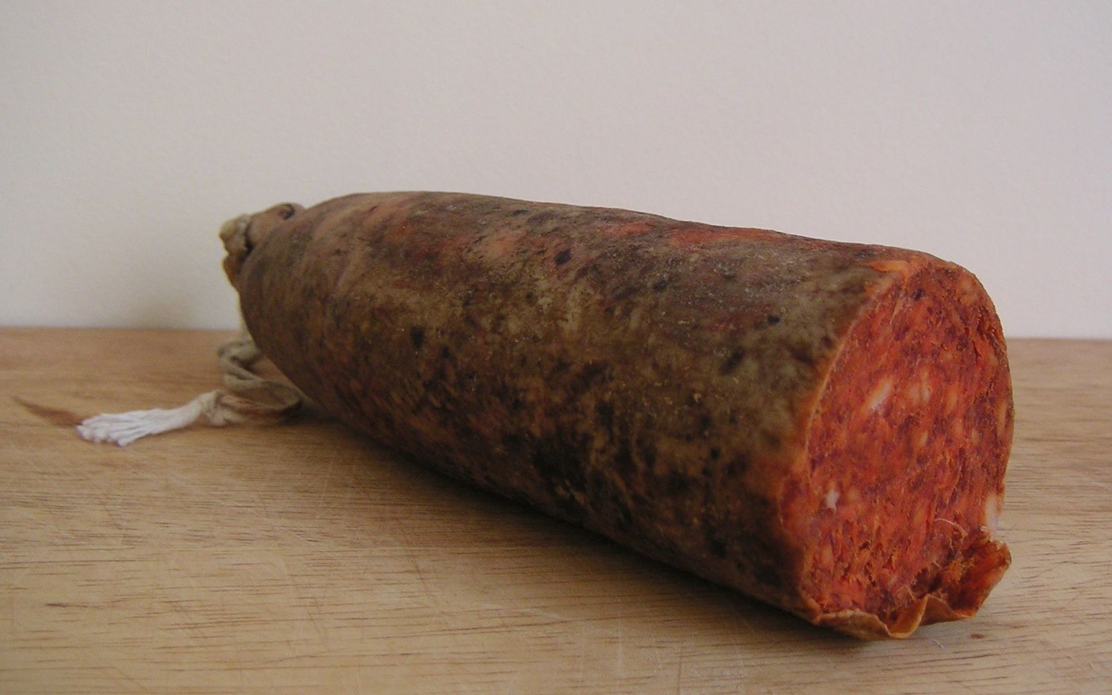 A cut sausage with a mottled casing and red cured meat interior on a wooden board