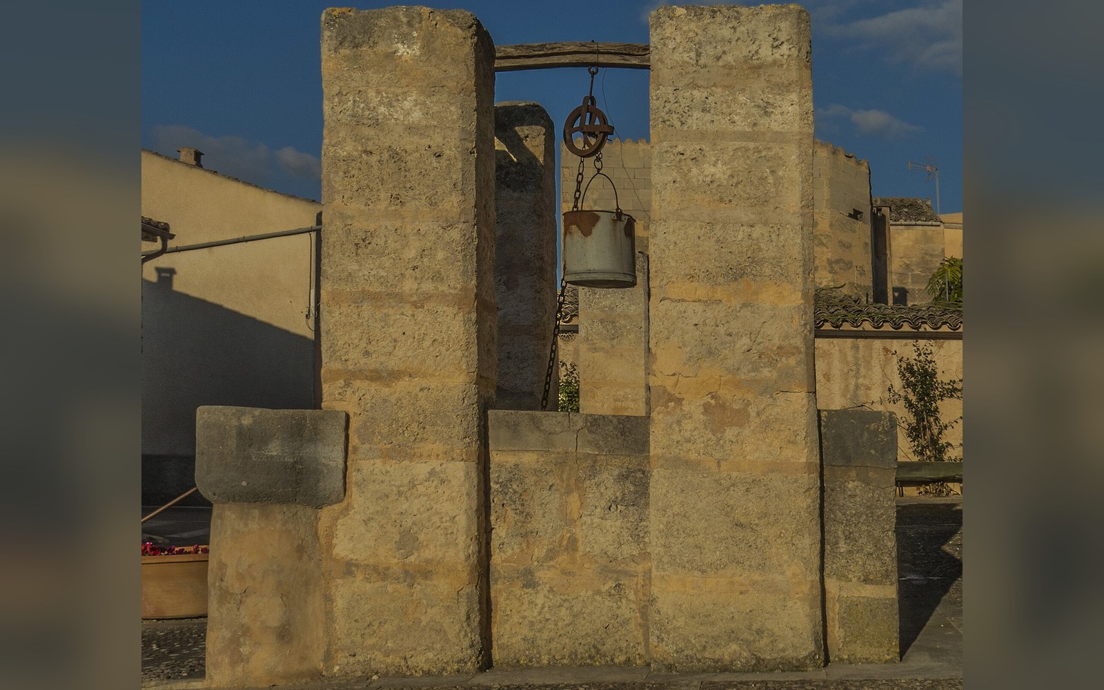 A stone well with a bucket suspended from an iron pulley between two pillars