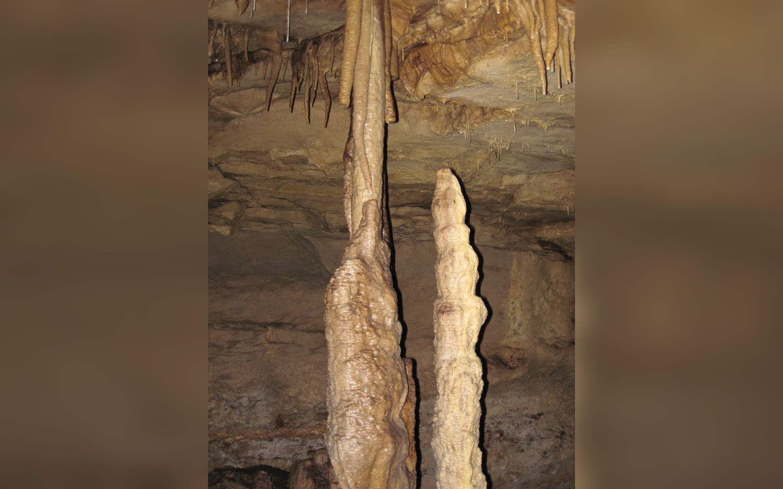 Two tall stalagmite columns rise from the cave floor beneath a ceiling of smaller stalactites
