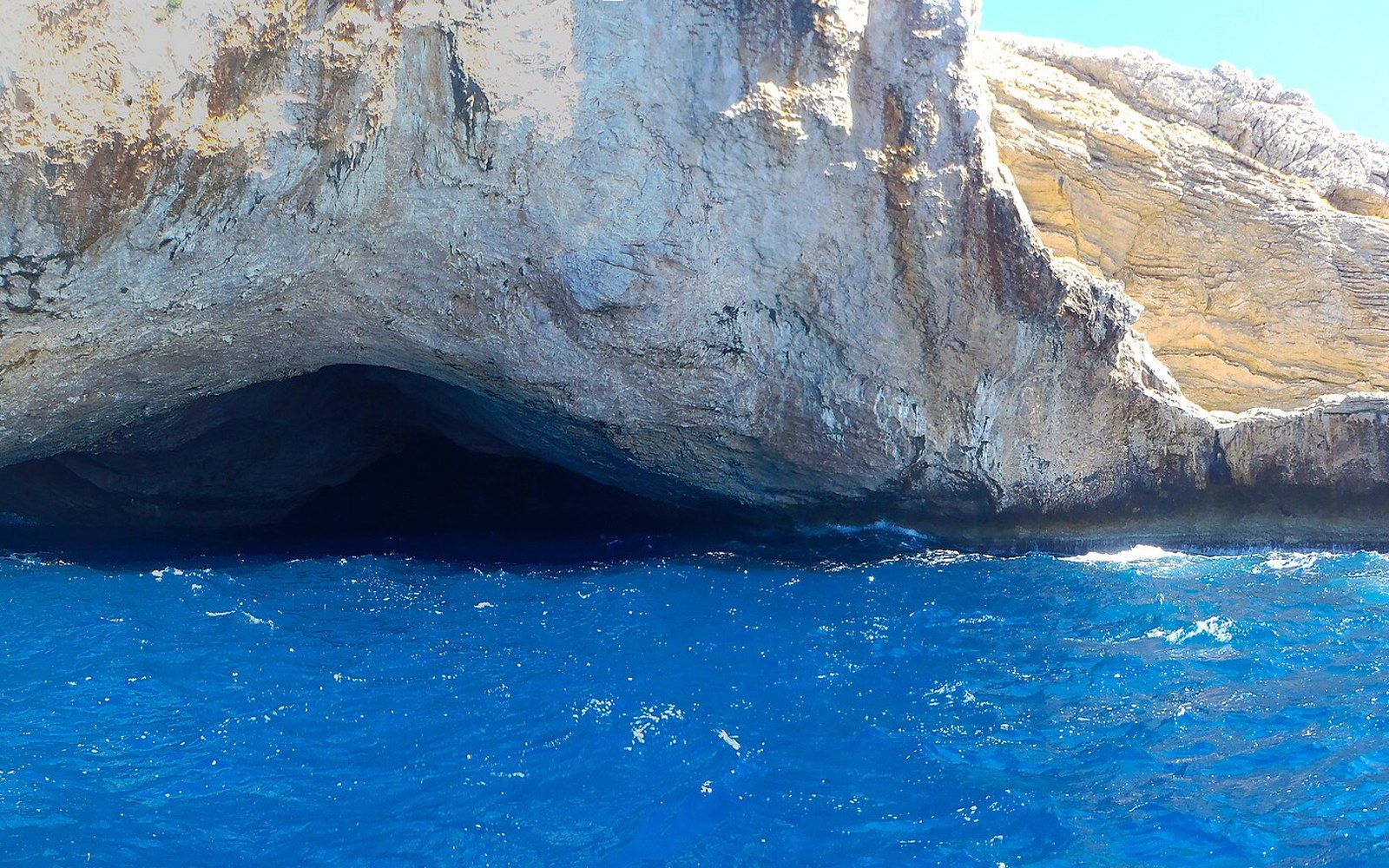 A sea cave entrance carved into a limestone cliff above deep blue water