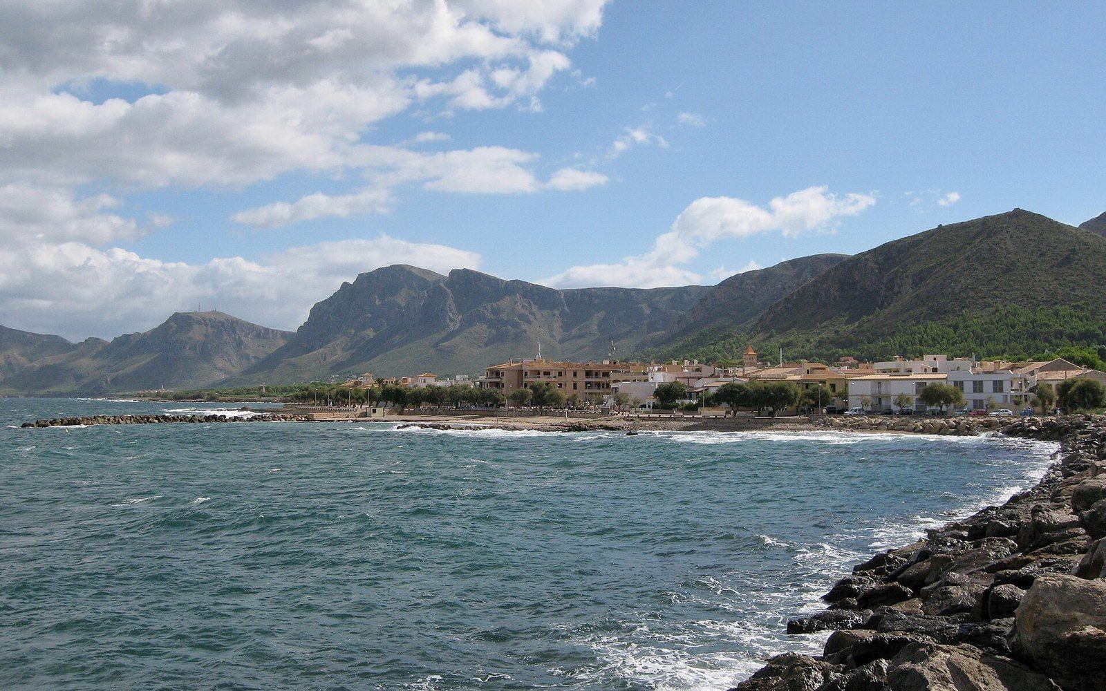 Coastal village of Colònia de Sant Pere hugs the shoreline beneath a mountain range